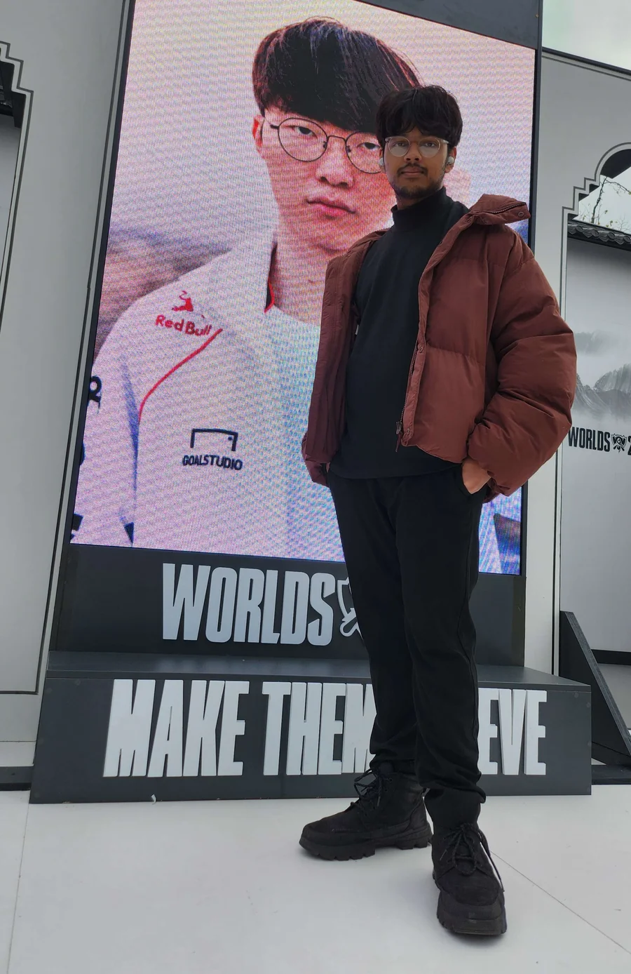 Mahin at the 2024 League of Legends Worlds Finals in London, in a brown puffer jacket in front of the Make Them Believe stage screen